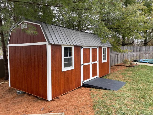 Red lofted barn shed with ramp in a backyard