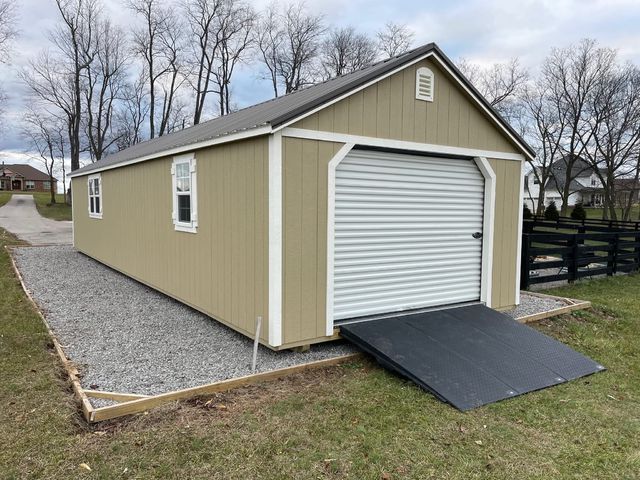 Tan portable garage with roll-up door on a gravel pad